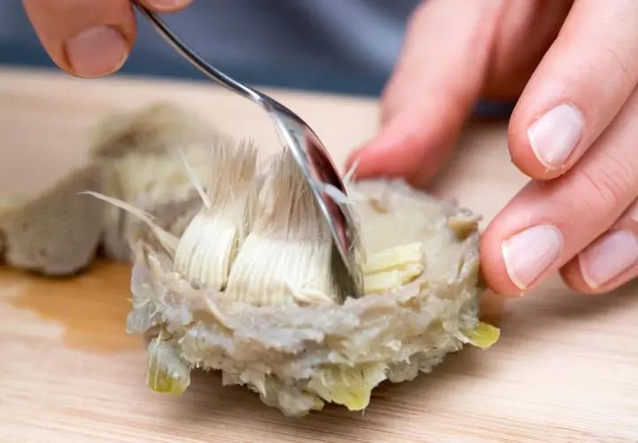 Mit einer Gabel wird das zarte Herz einer gekochten Artischocke freigelegt. So isst man Artischocken: Blatt für Blatt abziehen und das Fleisch abkratzen.