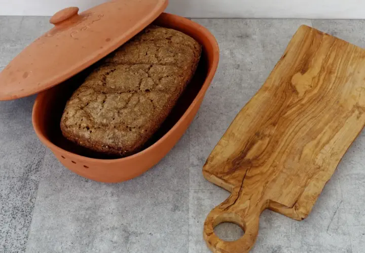 Ein Laib Brot liegt in einem Terrakotta-Brotbehälter. Daneben eine Holzschneidebrett. Perfekt, um Brot aufbewahren.