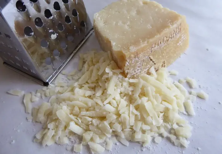Ein Stück Pecorino liegt neben frisch geriebenem Käse und einer Reibe. Der Kampf Pecorino vs Parmesan beginnt!