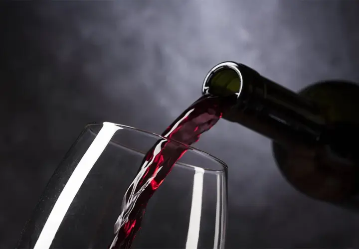 Rotwein fließt aus einer Flasche in ein Glas. Ist Wein vegan? Ja, dieser Wein ist vegan.