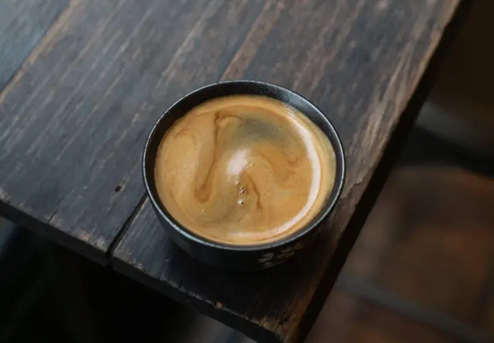 Ein dampfender americano kaffee mit schöner Crema in einer dunklen Tasse auf einem rustikalen Holztisch.