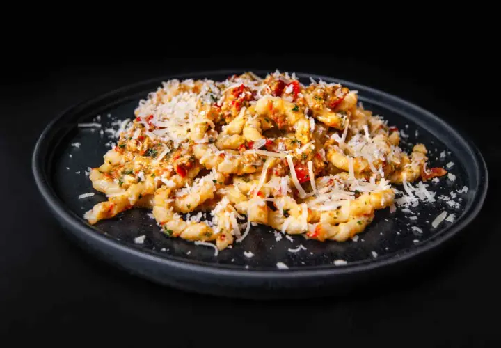 Gedrehte Pasta mit Pesto Trapanese, Tomaten und geriebenem Käse auf einem dunklen Teller.