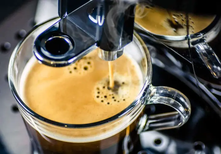 Frisch gebrühter Espresso fließt aus einem Vollautomaten in eine Glas Tasse. Der Kaffee schmeckt bitter, aber die Crema ist perfekt.