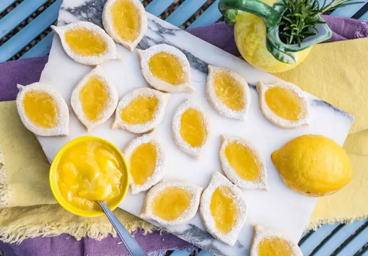 Zitronenkekse italienisch, mit leuchtend gelber Zitronencreme gefüllt und mit Puderzucker bestäubt, liegen auf einem Marmorbrett.