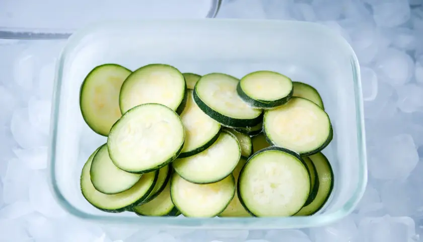 Scheiben von Zucchini lagern in einem Glasbehälter auf Eiswürfeln.