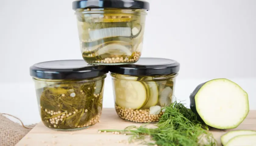 Drei Gläser mit eingelegtem Gemüse, bereit zum Einkochen im Weckglas. Zucchini, Zwiebeln und Dill sind mit Senfkörnern gefüllt.