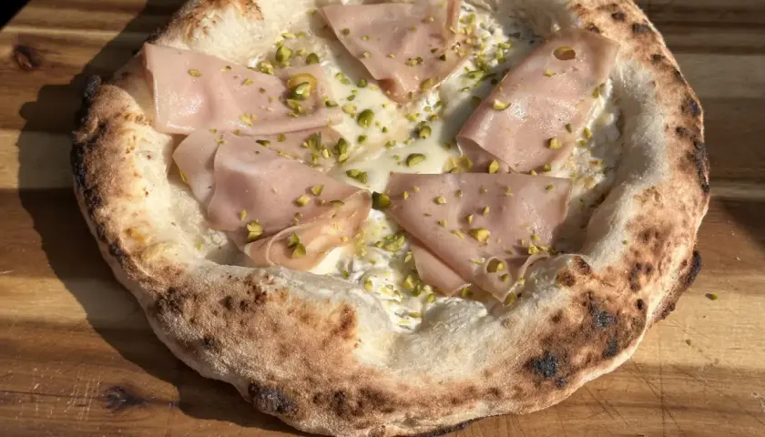 Pizza Napoletana mit Mortadella, Pistazien und cremiger Füllung auf einem Holzbrett.