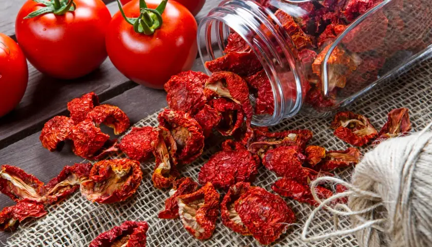 Frische Tomaten neben einem Glas mit getrockneten Tomaten und einem Garnknäuel. Die Zubereitung von Tomaten trocknen für den Winter.