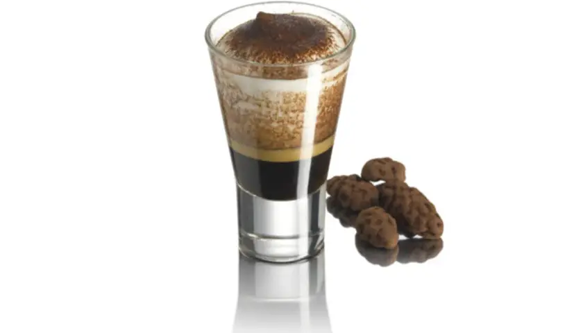 Ein Caffe Marocchino mit cremigem Schaum und Kakaopulver, daneben ein paar schokoladige Pralinen.