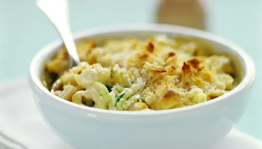 Ein cremiger Tortellini Zucchini Auflauf mit knuspriger Käsekruste, serviert in einer weißen Schüssel.