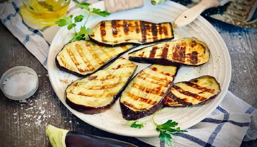 Gegrillte Aubergine-Scheiben mit Grillstreifen, garniert mit Petersilie, daneben Salz und Öl.