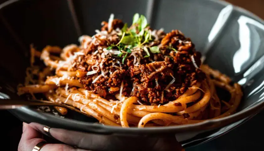 Eine Schüssel mit herzhaftem Pasta Ragu, garniert mit frischen Kräutern und geriebenem Käse.