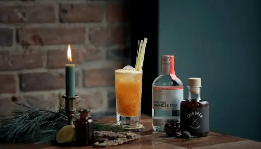 Ein erfrischender Kaffee Cocktail mit Wodka und Cold Brew, garniert mit Zitronengras. Kerzenlicht und Tannenzweige schaffen eine gemütliche Atmosphäre.