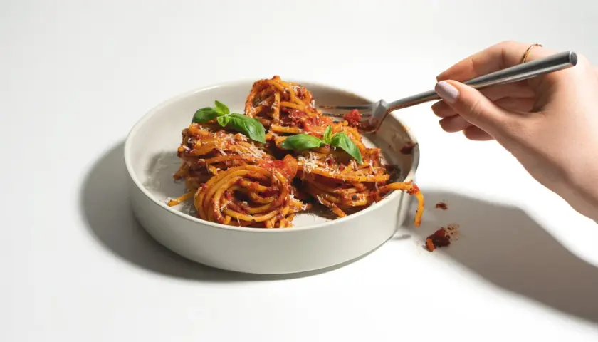 Ein Teller mit Spaghetti, garniert mit Basilikum und Parmesan. Verschiedene Nudel-Sorten sind hier als köstliche Mahlzeit präsentiert.