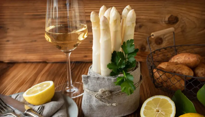 Ein Glas Weißwein neben frischem Spargel, Kartoffeln und Zitronen. Die perfekte Kombination, um die Frage zu beantworten: welchen Wein zu Spargel.
