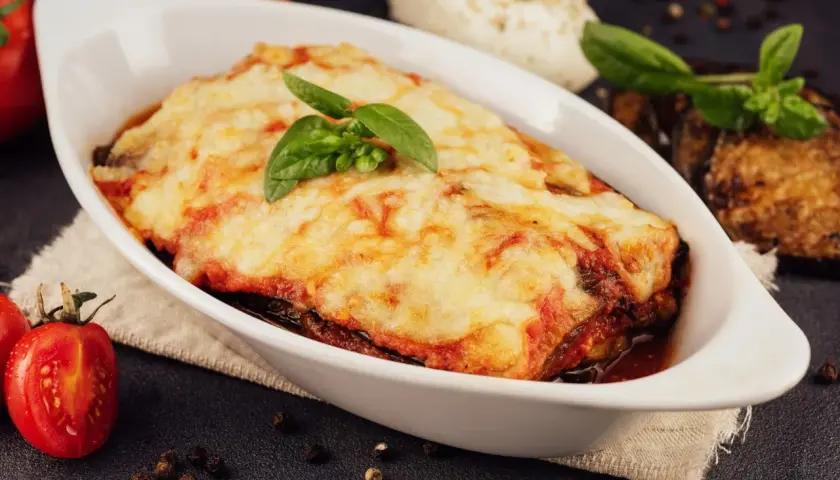 Herzhafte Auberginen Lasagne mit geschmolzenem Käse und frischem Basilikum, serviert in einer weißen Auflaufform.