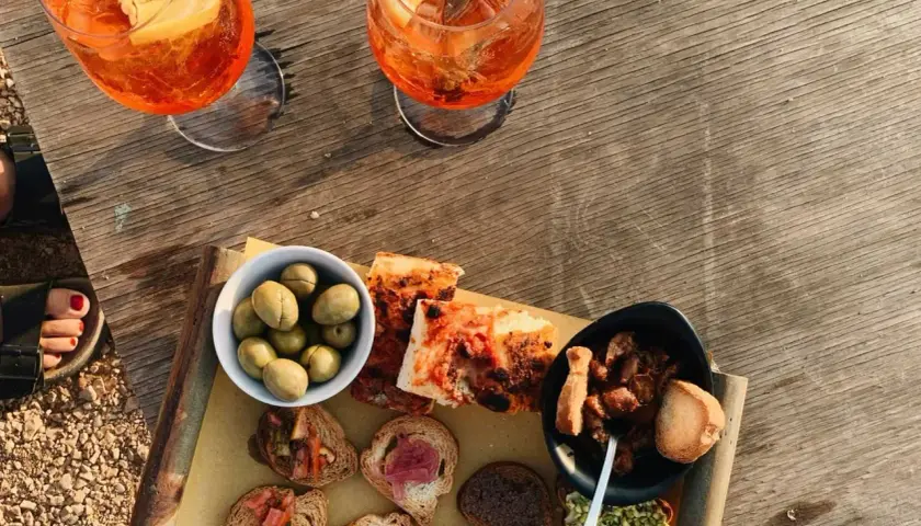 Zwei Aperol Spritz und eine Auswahl an italienischen Aperitif-Spezialitäten: Oliven, Bruschetta und Pizza.