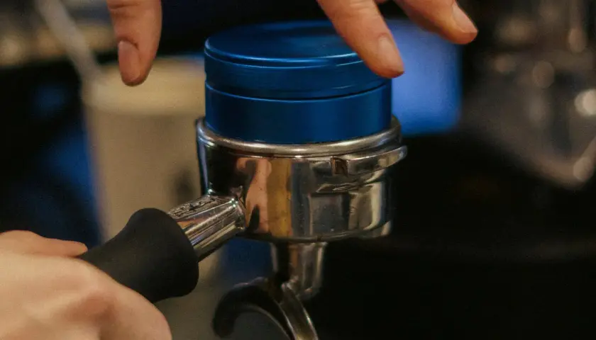 Barista bereitet Espresso zu, indem er den Tamper auf den Kaffeepuck im Siebträger drückt.