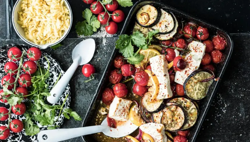 Ofenfrisches Gericht mit Aubergine, Tomaten und Feta. Dazu Orzo-Nudeln und frische Kräuter.