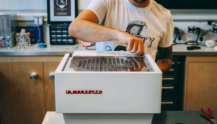 Mann reinigt eine La Marzocco Espressomaschine. Sorgfältige Pflege für perfekten Kaffeegenuss.