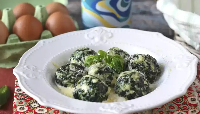 Malfatti rezept: Grüne, käsige Klößchen mit Spinat und Basilikum auf einem Teller, daneben Eier im Karton.