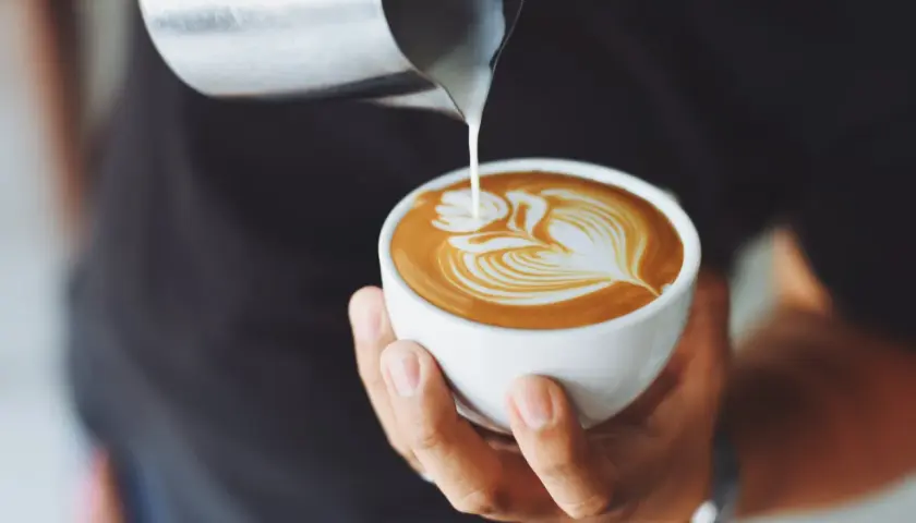 Ein Barista gießt Milch in eine Tasse, um ein Latte Art Muster zu kreieren. Ein perfekter Kaffee auf italienisch.