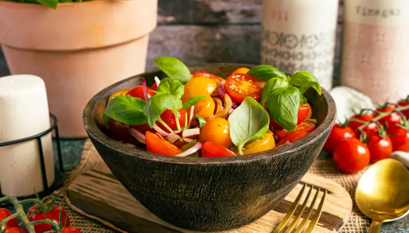 Frischer Tomatensalat italienisch mit Basilikum, Zwiebeln und Kirschtomaten in einer Holzschale.
