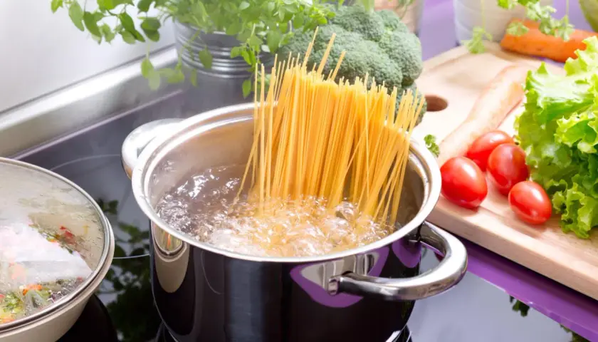 Spaghetti kochen: Lange Nudeln im sprudelnden Wasser, daneben frisches Gemüse wie Brokkoli, Tomaten und Salat.