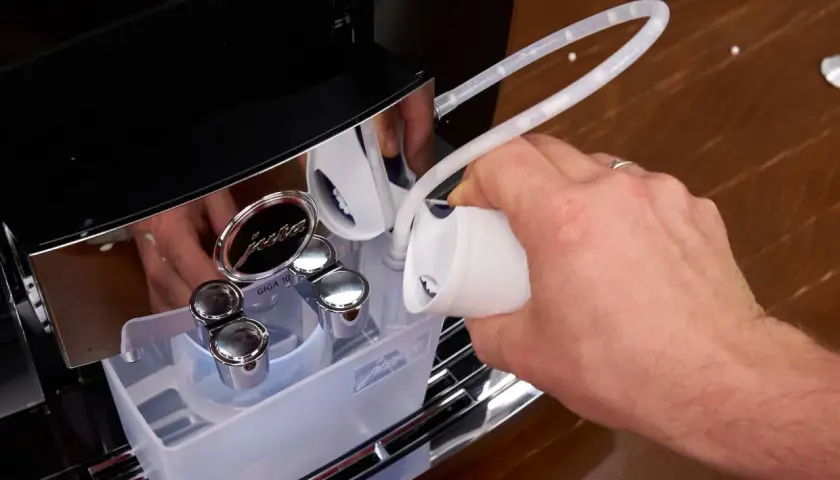 Hand füllt Entkalkungsmittel in eine Jura Kaffeemaschine. Regelmäßiges Entkalken sorgt für Langlebigkeit.