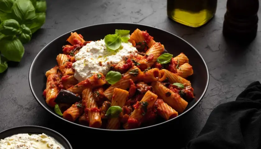Rigatoni mit Auberginen-Tomaten-Sauce und cremigem Ricotta – ein Beweis für die besten Rezepte mit Auberginen. Frischer Basilikum und Olivenöl runden das Gericht ab.