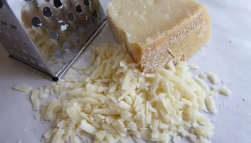 Ein Stück Pecorino liegt neben frisch geriebenem Käse und einer Reibe. Der Kampf Pecorino vs Parmesan beginnt!