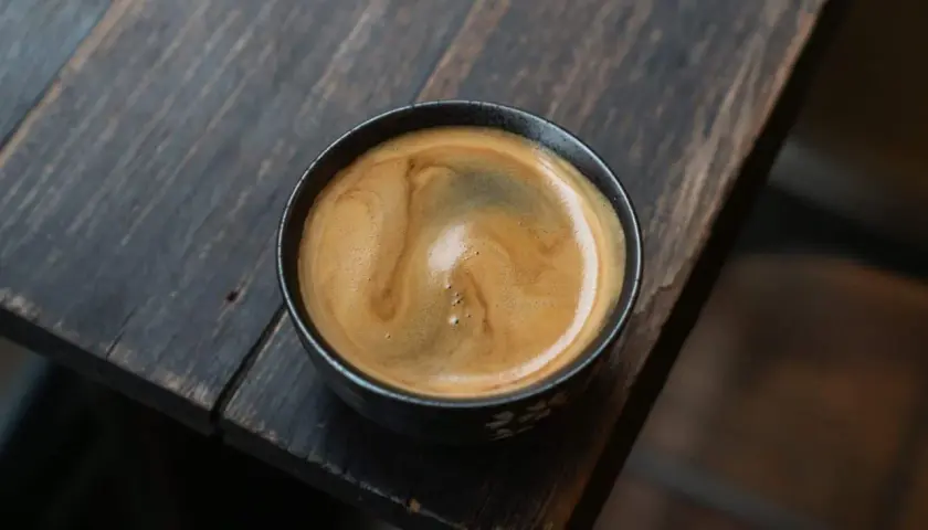 Ein dampfender americano kaffee mit schöner Crema in einer dunklen Tasse auf einem rustikalen Holztisch.