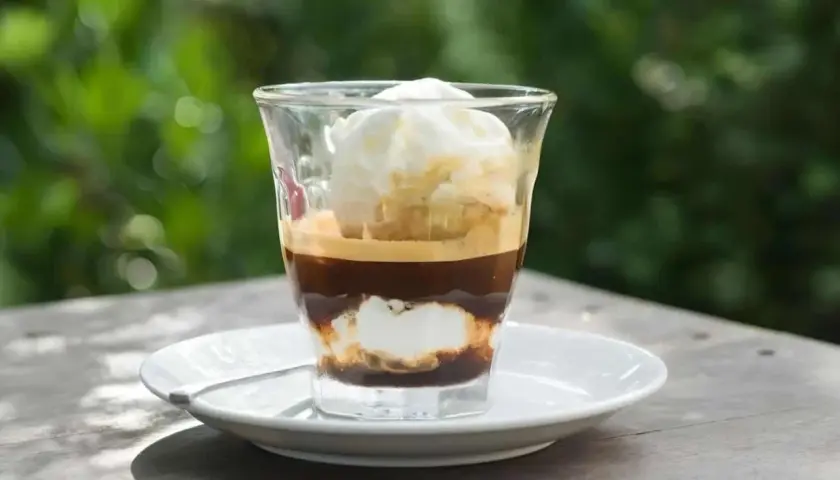 Ein Glas mit Espresso und Vanilleeis, das auf einem Tisch im Freien steht.