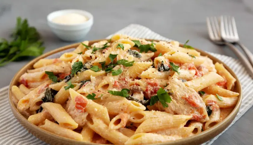 Cremige Penne mit sonnengetrockneten Tomaten, Spinat und Parmesan, garniert mit frischer Petersilie. Ein köstliches Gericht, das Lust auf mehr macht.