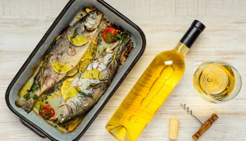 Zwei gebackene Forellen mit Zitrone und Kräutern, daneben eine Flasche Weißwein und ein Glas. Perfekt, welcher Wein zu Fisch passt!