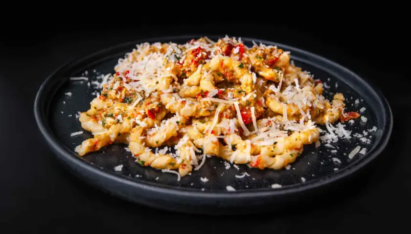 Gedrehte Pasta mit Pesto Trapanese, Tomaten und geriebenem Käse auf einem dunklen Teller.