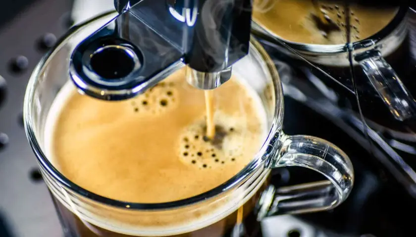 Frisch gebrühter Espresso fließt aus einem Vollautomaten in eine Glas Tasse. Der Kaffee schmeckt bitter, aber die Crema ist perfekt.