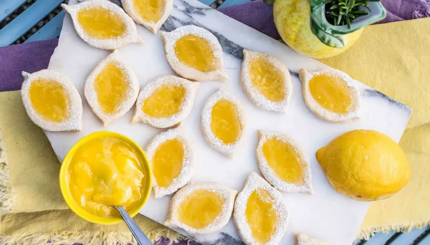 Zitronenkekse italienisch, mit leuchtend gelber Zitronencreme gefüllt und mit Puderzucker bestäubt, liegen auf einem Marmorbrett.