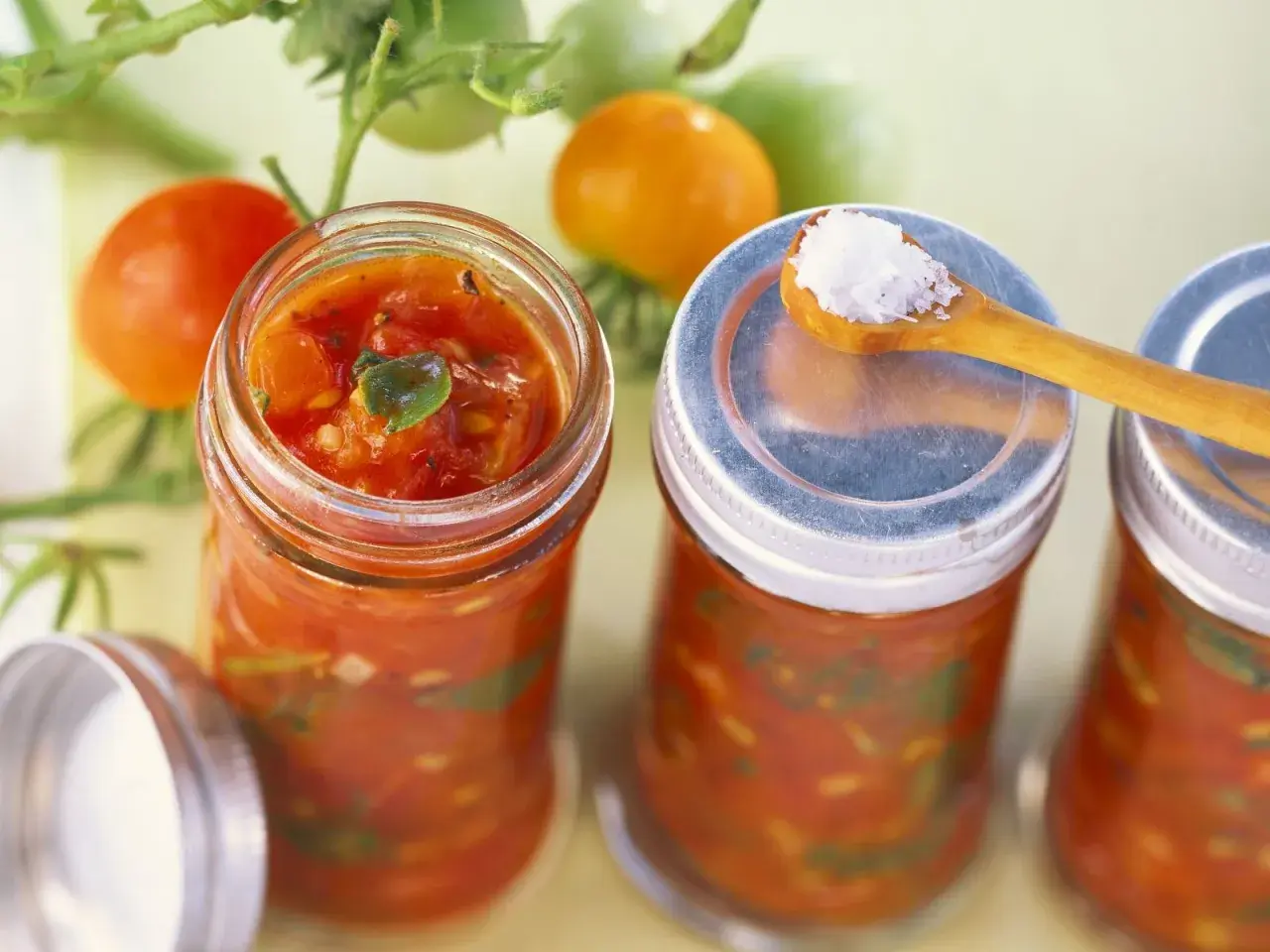 Frische Tomaten und Gläser mit Tomaten-Salsa, perfekt für leckere Tomaten Rezepte. Eine Löffelspitze Salz liegt bereit.