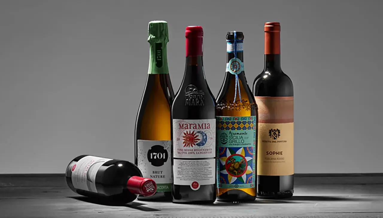 Fünf Flaschen Wein, darunter ein Sekt und vier Rotweine, stehen auf einem Tisch. Einer der Rotweine liegt. Ein Etikett weist auf biodynamischen Wein hin.