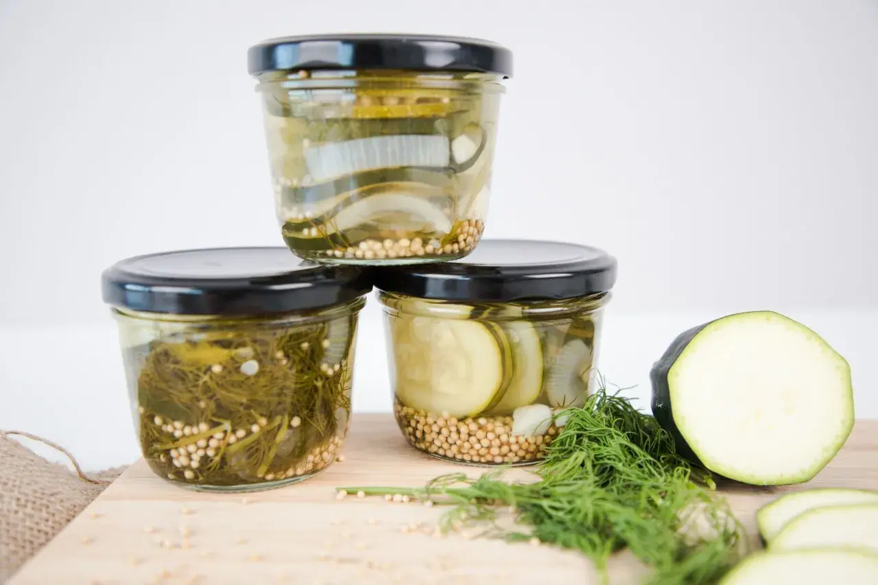 Drei Gläser mit eingelegtem Gemüse, bereit zum Einkochen im Weckglas. Zucchini, Zwiebeln und Dill sind mit Senfkörnern gefüllt.