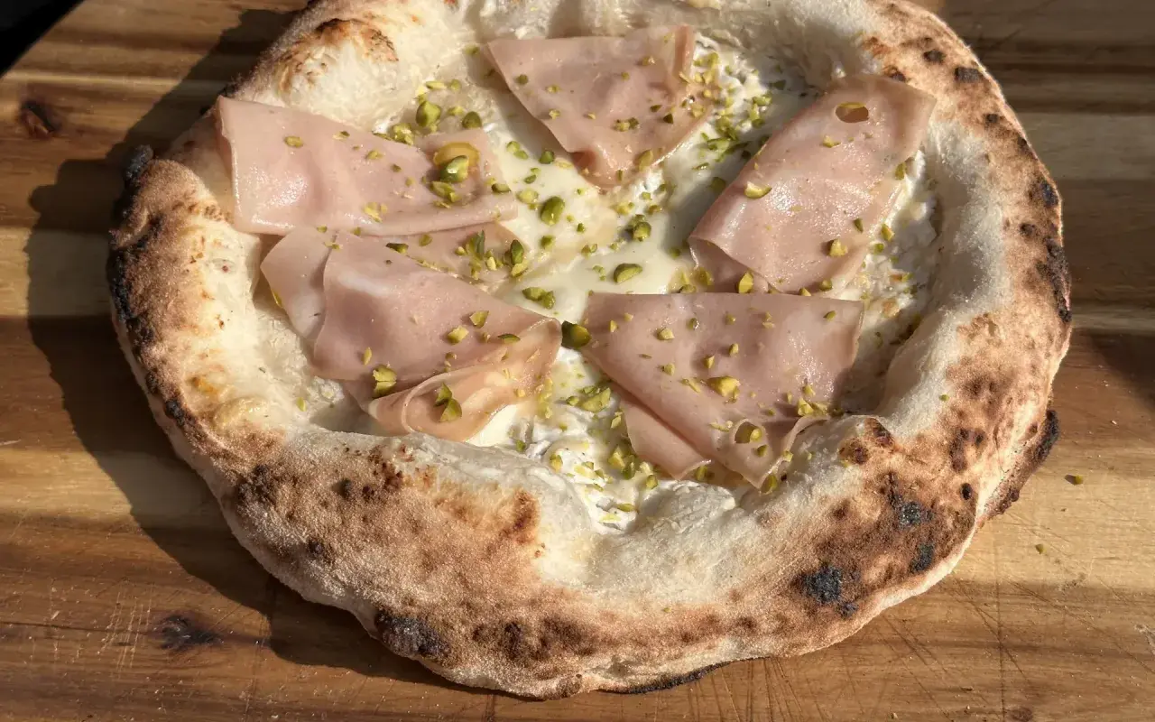 Pizza Napoletana mit Mortadella, Pistazien und cremiger Füllung auf einem Holzbrett.