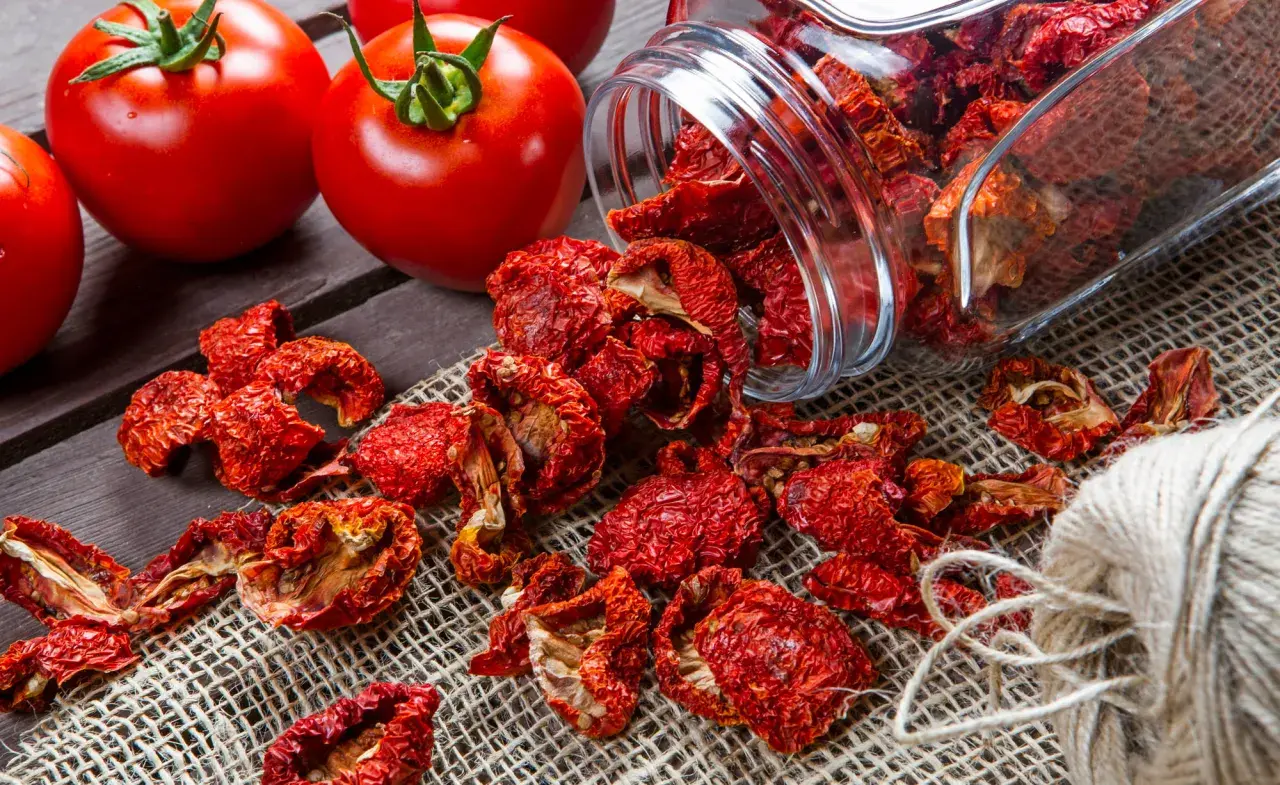 Frische Tomaten neben einem Glas mit getrockneten Tomaten und einem Garnknäuel. Die Zubereitung von Tomaten trocknen für den Winter.