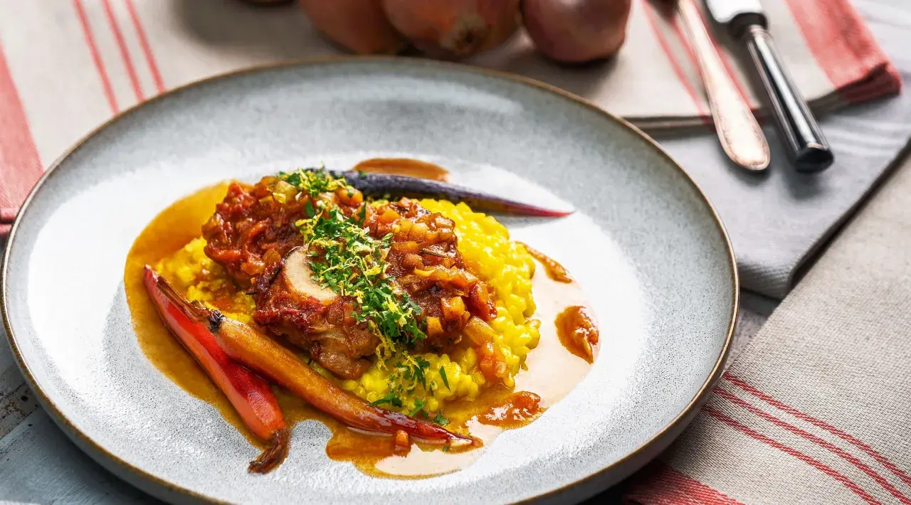 Ein köstliches Ossobuco Rezept mit zartem Kalbfleisch, serviert auf Safranrisotto und garniert mit frischen Kräutern und karamellisierten Karotten.
