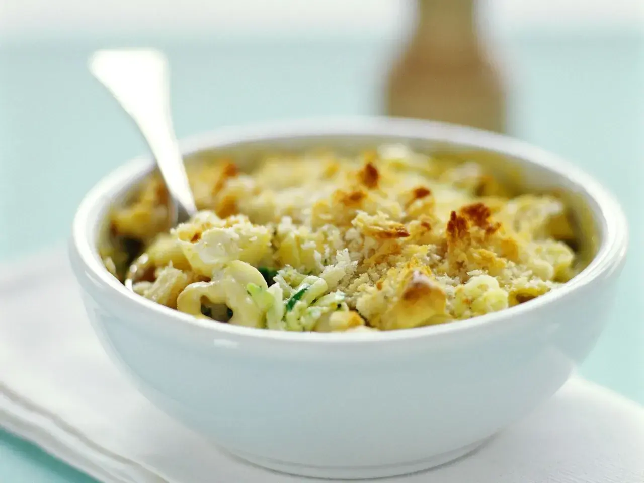 Ein cremiger Tortellini Zucchini Auflauf mit knuspriger Käsekruste, serviert in einer weißen Schüssel.