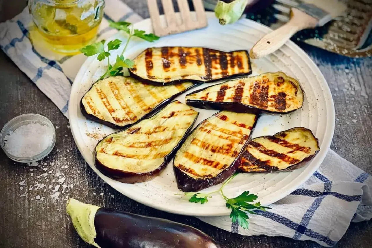 Gegrillte Aubergine-Scheiben mit Grillstreifen, garniert mit Petersilie, daneben Salz und Öl.