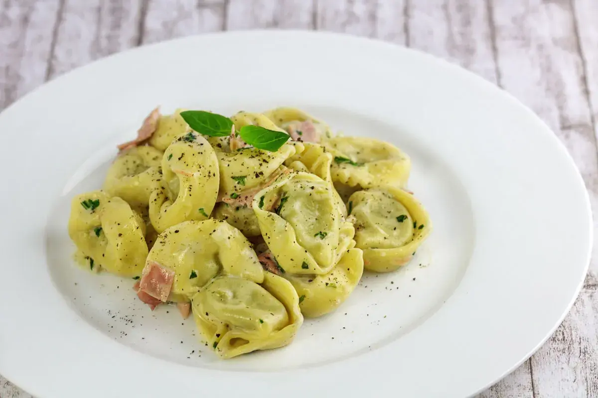 Spinat Ricotta Tortellini in cremiger Sauce, garniert mit Basilikum und schwarzem Pfeffer. Ein köstliches Gericht, das zum Genießen einlädt.