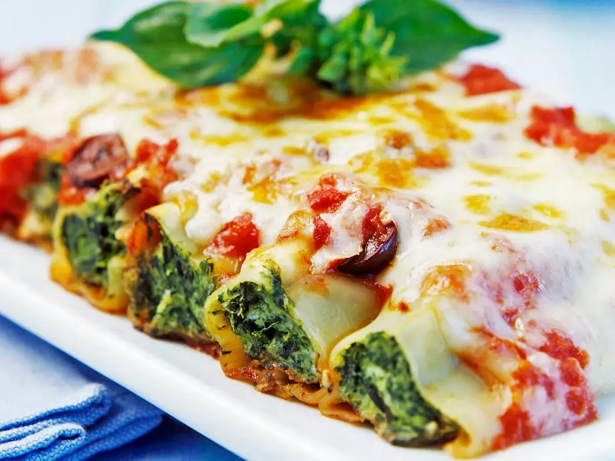 Cannelloni gefüllt mit Spinat und Ricotta, überbacken mit Tomatensauce und Käse, garniert mit Basilikum.