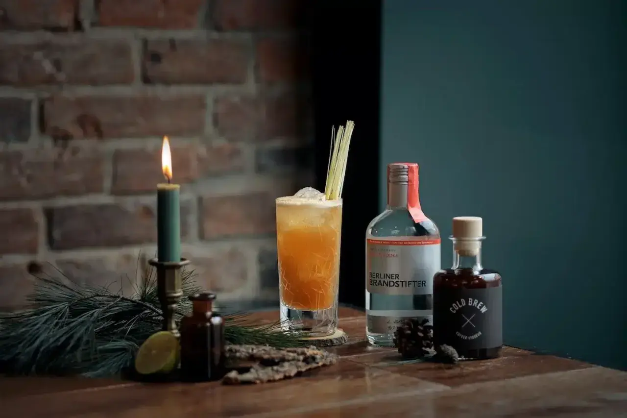 Ein erfrischender Kaffee Cocktail mit Wodka und Cold Brew, garniert mit Zitronengras. Kerzenlicht und Tannenzweige schaffen eine gemütliche Atmosphäre.