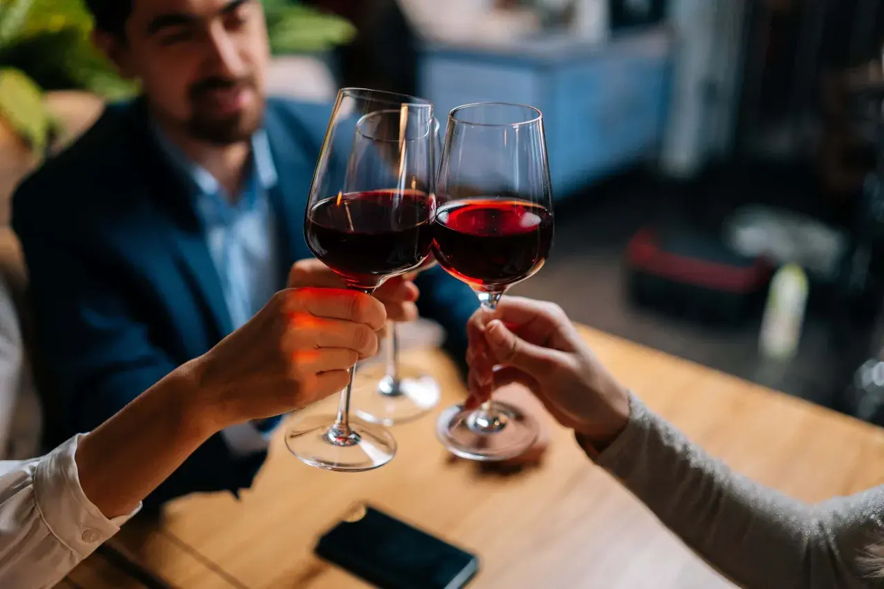 Drei Personen stoßen mit Rotwein an. Sie halten das weinglas richtig, am Stiel, um die Temperatur des Weins zu bewahren.
